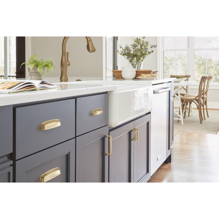 a kitchen with gray cabinets and gold pulls on the handles, an open book is sitting on the counter