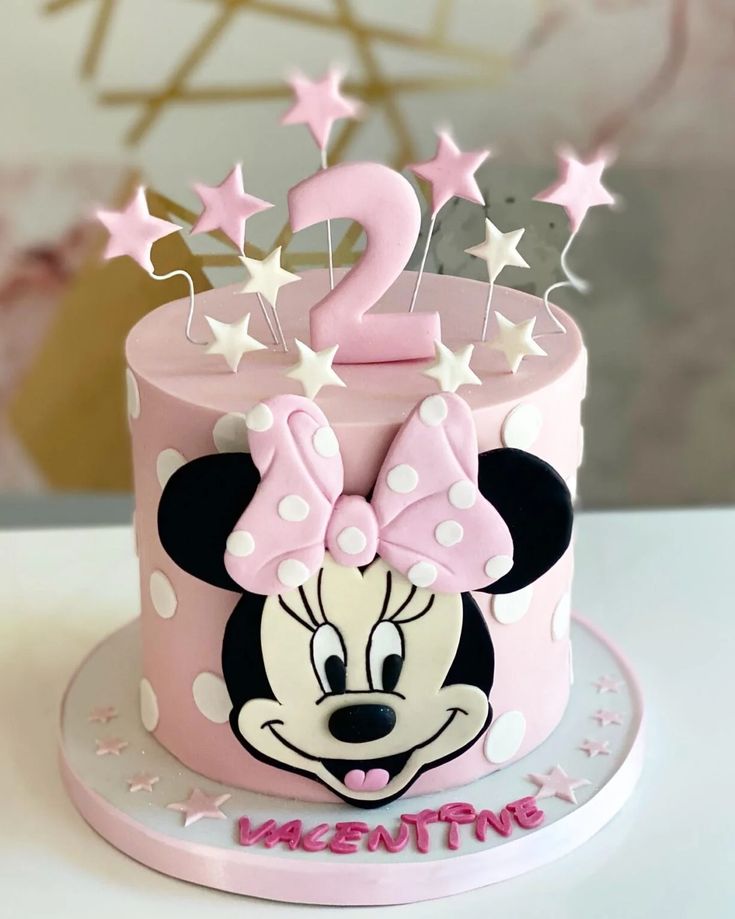 a pink and white cake with minnie mouse on it's top, decorated with stars