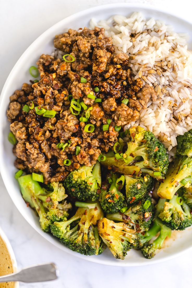 a white bowl filled with meat and broccoli on top of a marble counter