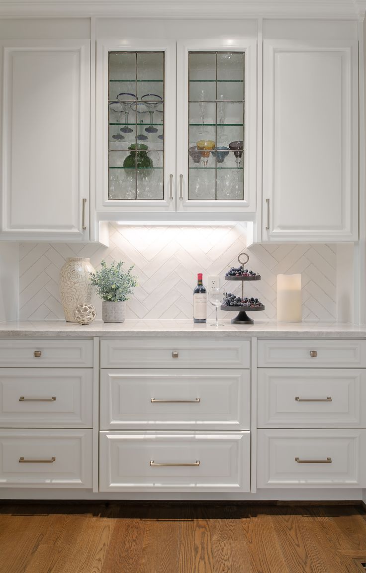 a kitchen with white cabinets and wood flooring, glass front cupboards on the wall