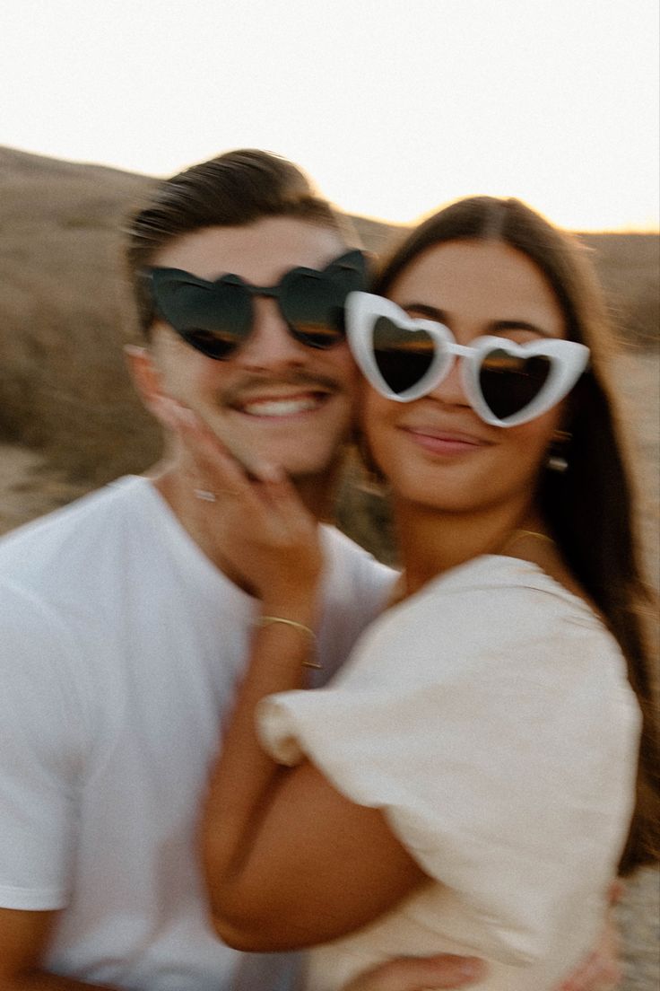 a man and woman wearing heart - shaped sunglasses pose for a photo in the desert