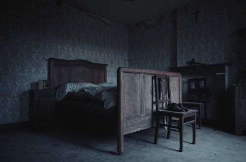 a dark room with a bed, night stand and table in the corner next to it