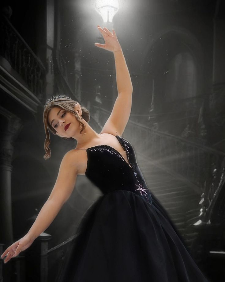 a woman in a black dress is holding her hand up to the light on top of a staircase