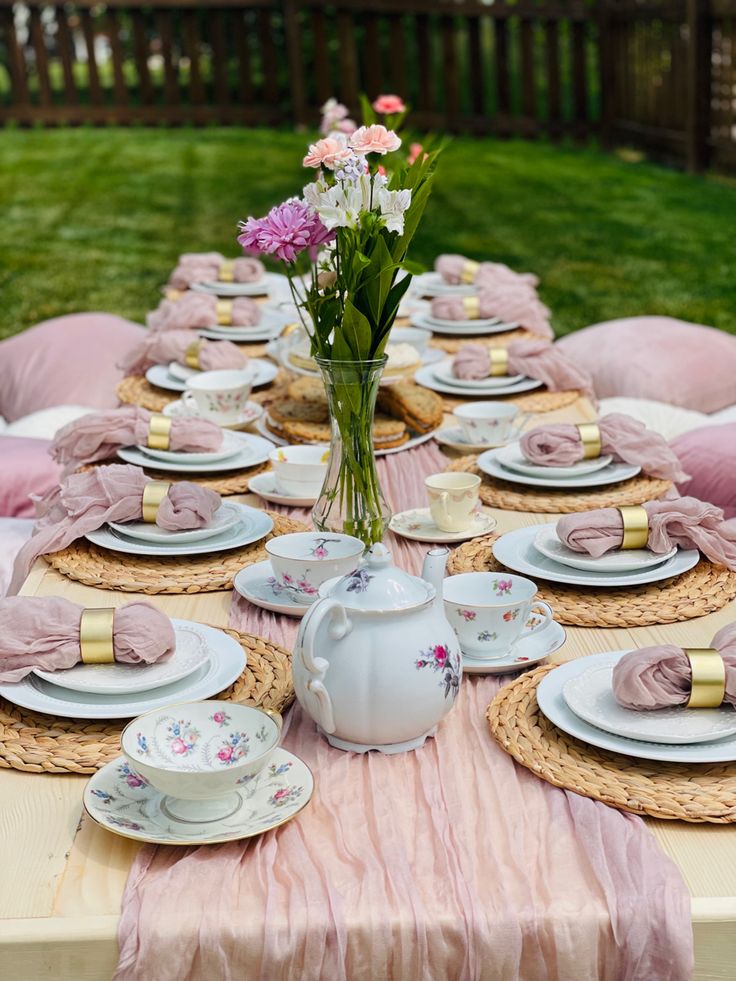 the table is set with pink and white plates, cups, and flowers in vases