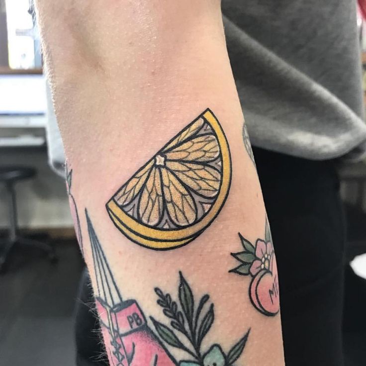 a close up of a person's arm with a tattoo on it and an orange slice