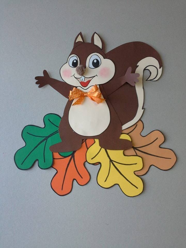 a paper cutout of a squirrel on top of leaves and acorns with an orange bow tie