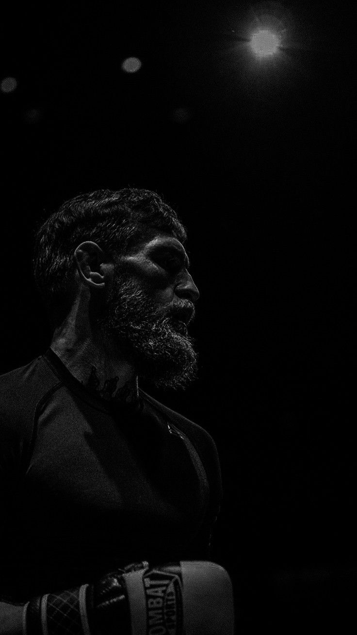 a man standing in the dark with his arm wrapped around his chest and wearing boxing gloves