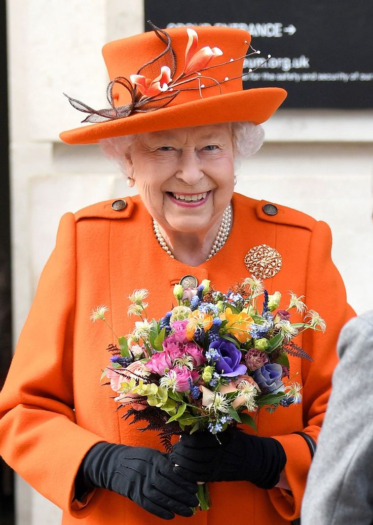 the queen is holding a bouquet of flowers in her hand and wearing an orange coat