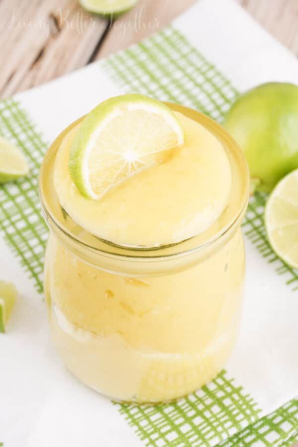 a glass jar filled with lemonade and limes on top of a napkin next to some sliced limes