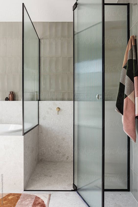 a bathroom with a glass shower door and tiled walls, along with a rug on the floor