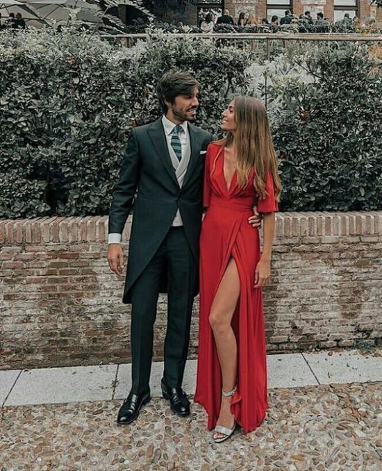 a man and woman standing next to each other in front of a brick wall with bushes