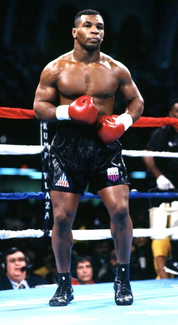 a man standing next to a boxing ring wearing red and white gloves with his hands on his hips