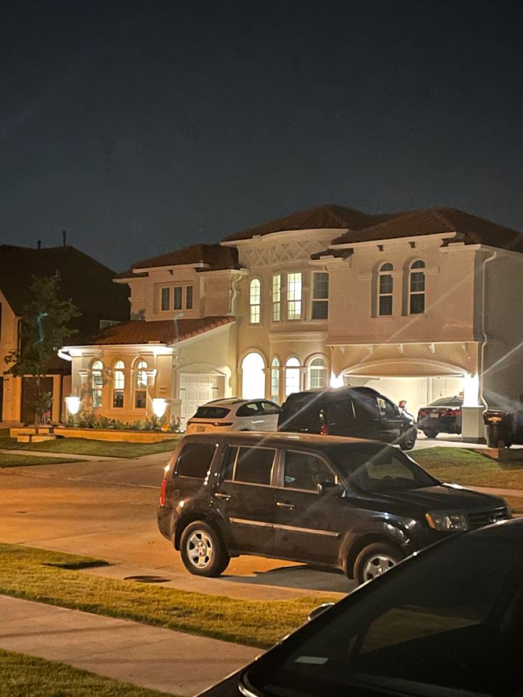 several cars parked in front of a large house at night with the lights turned on