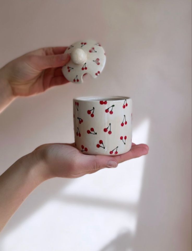 a hand holding a cup with cherries on it and a small white object in the middle