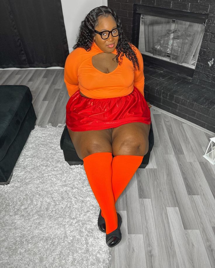 a woman in an orange top and red skirt sitting on the floor with her legs crossed