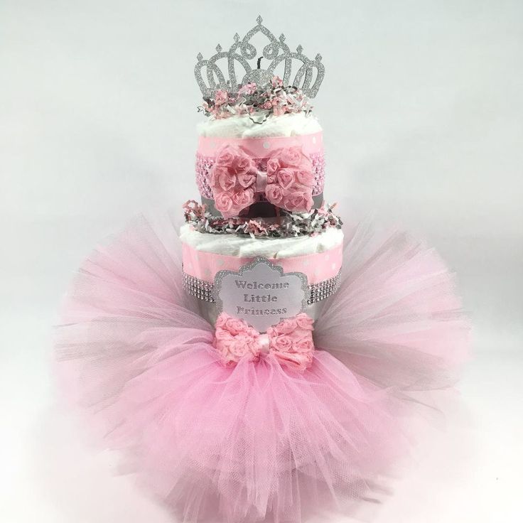 two tiered cake decorated with pink flowers and a tiara on top, sitting in front of a white background