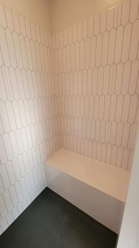 the corner of a room with a bench and tiled wall behind it in an empty space