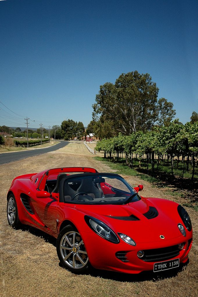 a red sports car parked on the side of a dirt road in front of trees