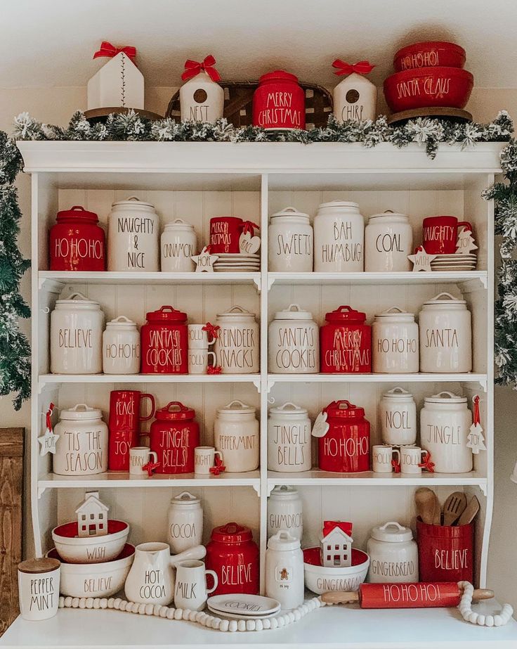 a shelf filled with red and white kitchenware on top of a table next to a christmas tree