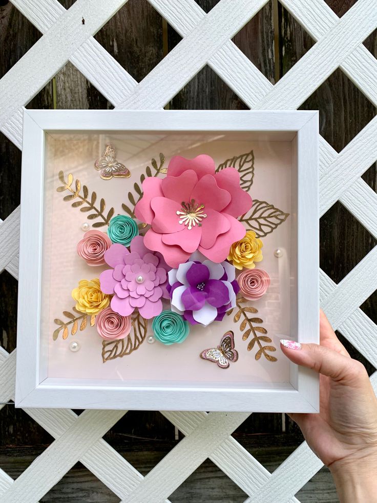 a person holding up a shadow box with paper flowers in it