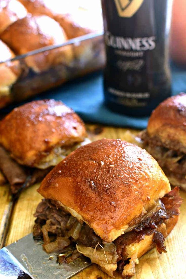 the sandwich is cut in half on the cutting board with a bottle of guinness next to it