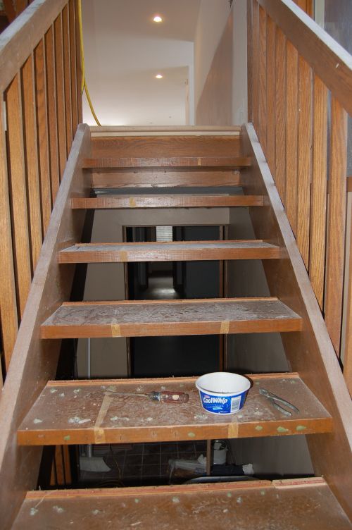 a bucket of paint sitting on the bottom of a wooden stair case in an unfinished room