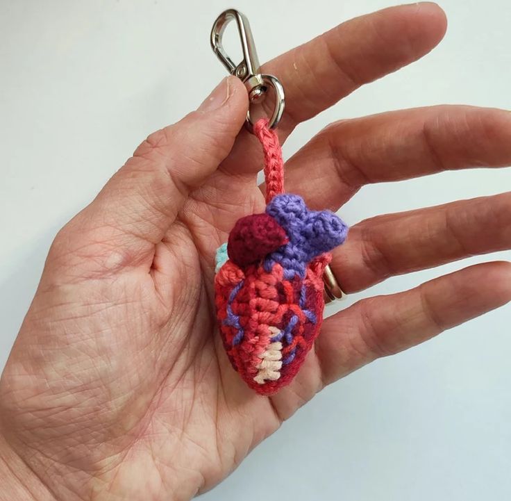 a hand holding a small crocheted heart keychain in it's palm