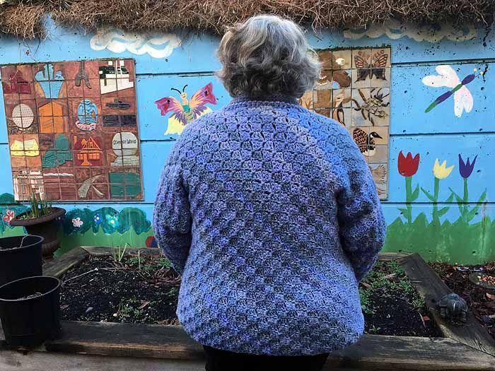 an older woman standing in front of a colorful wall with flowers and butterflies painted on it