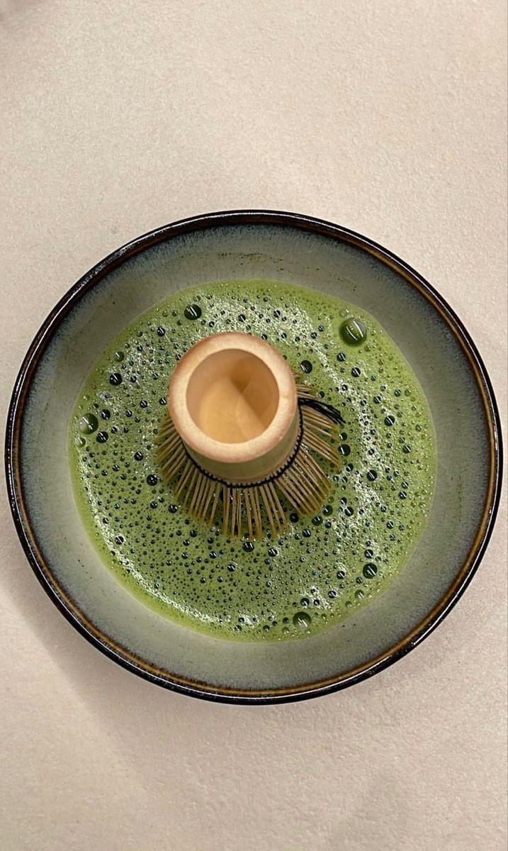 a green and black dish with a brush in the center on a white tablecloth