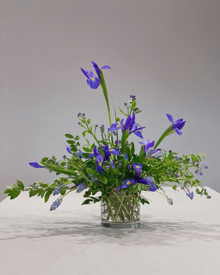 a glass vase filled with blue flowers on top of a white tablecloth covered table