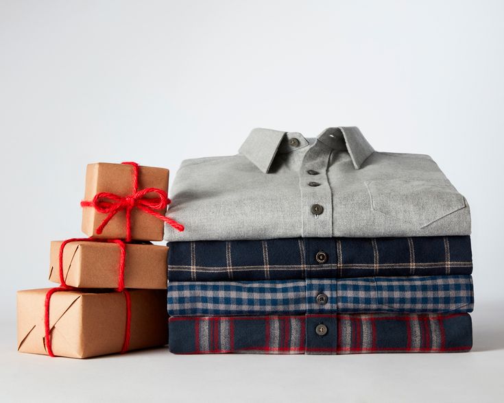 a stack of folded shirts and boxes with red ribbon tied around the collar, on white background