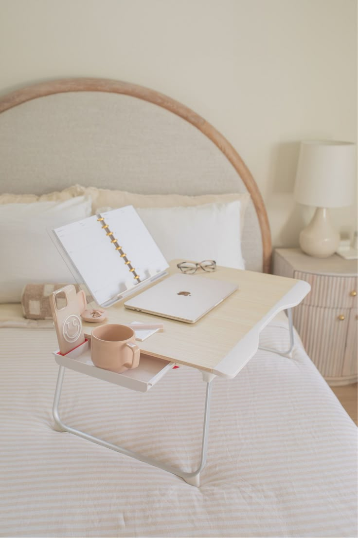 a white bed topped with a wooden table next to a night stand and cup filled with coffee