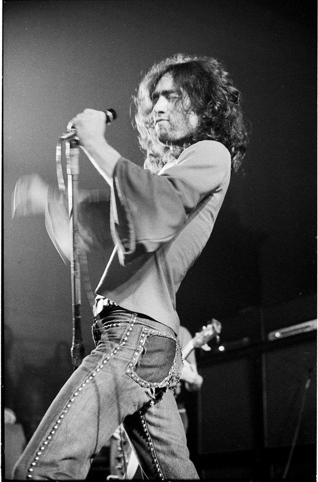 a black and white photo of a man with long hair on stage holding a microphone