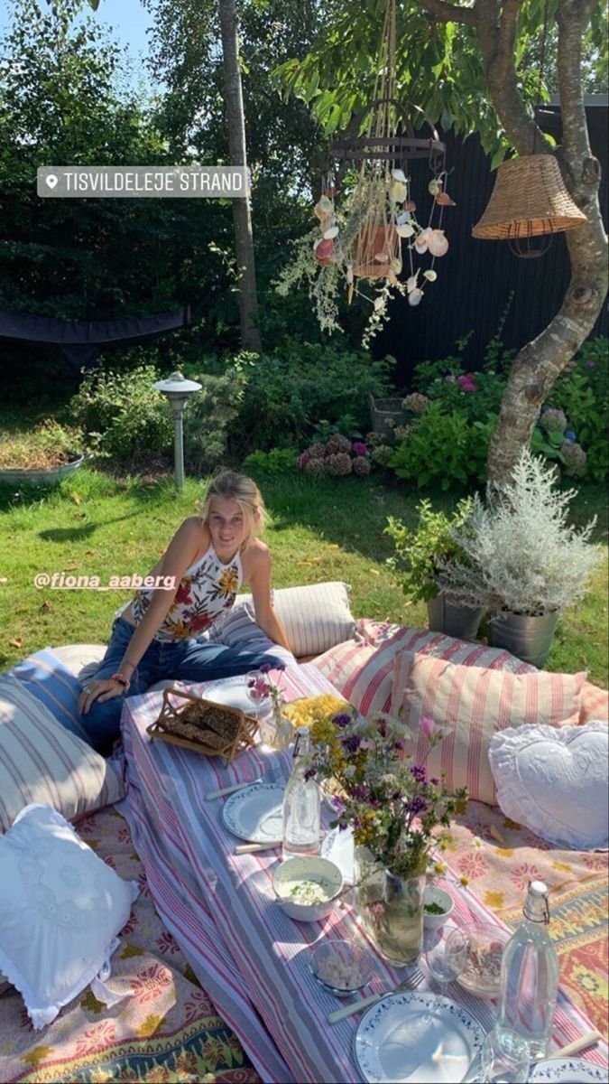 a woman sitting on top of a blanket in the middle of a yard next to a tree