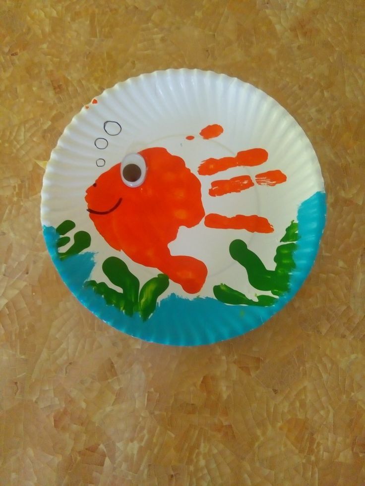 a paper plate with an image of a handprinted orange fish on it, sitting on a table