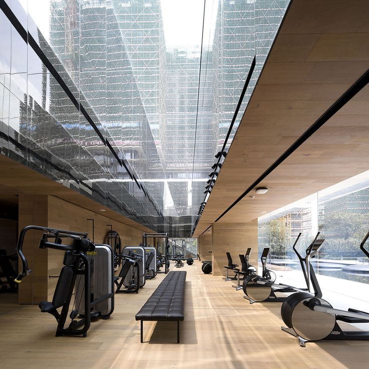 there are many exercise machines in this large room with wood flooring and glass walls