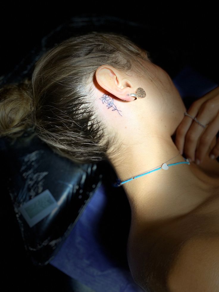 a woman with a small tattoo on her left side of her neck and behind her ear