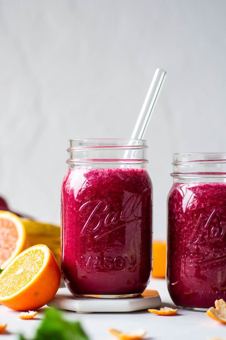 two mason jars filled with smoothie next to sliced oranges