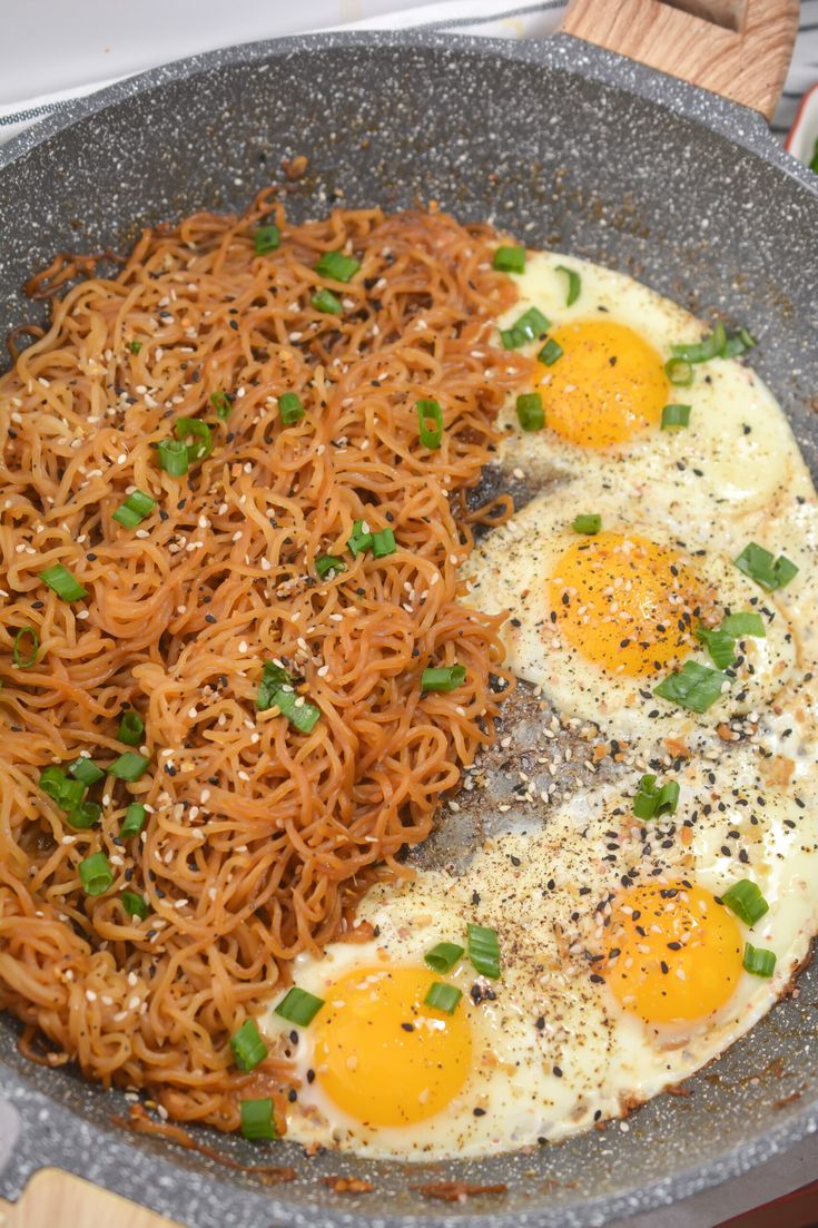 two fried eggs on top of noodles in a frying pan