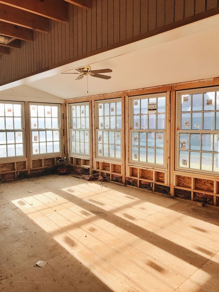 an empty room with several windows and wood framing on the walls, in front of a ceiling fan