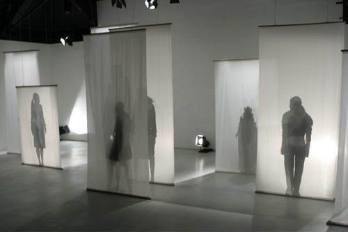 several people are standing in front of white walls with light coming through the windows and shadows on them