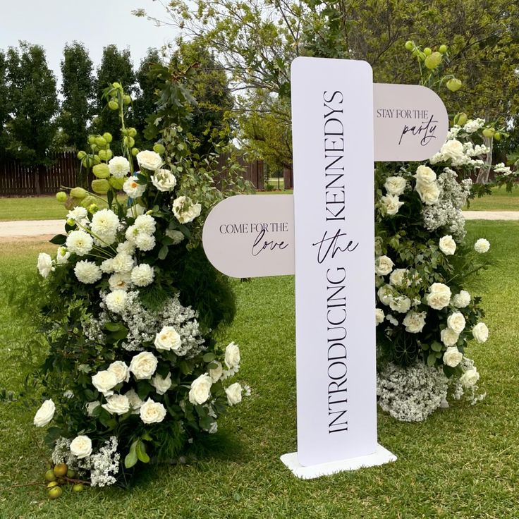 two white flowers are on the grass next to a sign that says, wedding ceremony