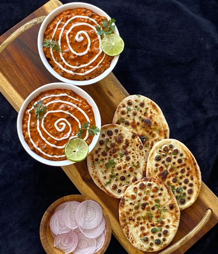 three bowls of soup and some pita bread on a wooden platter with onion rings