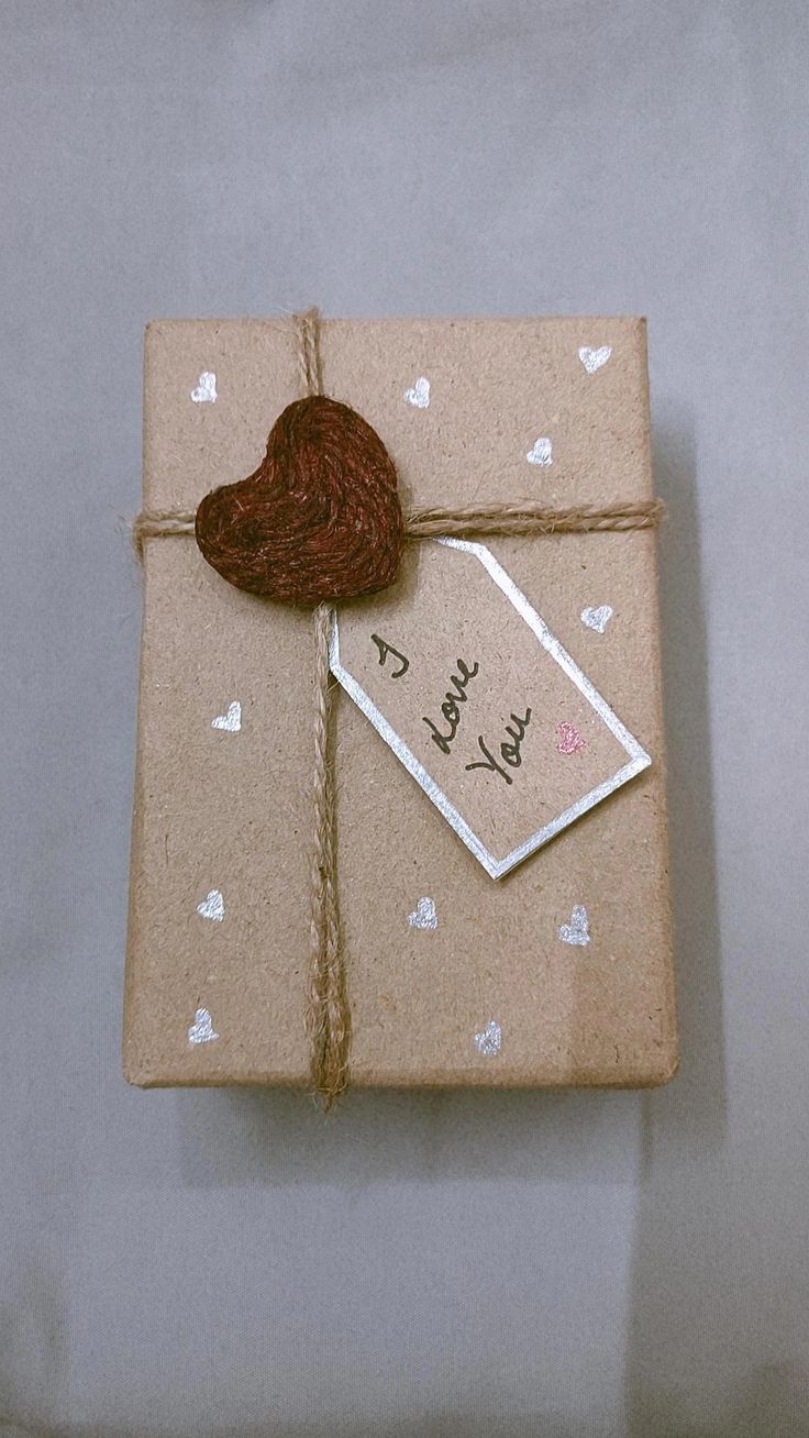 a brown wrapped gift with a heart on it's side and a tag attached to the top