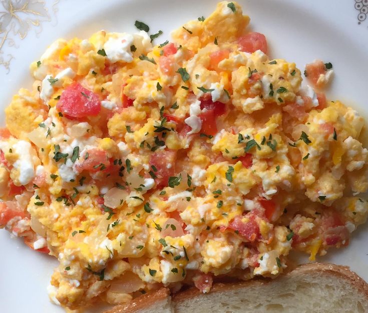 an egg salad on a white plate next to a slice of bread with cheese and tomatoes