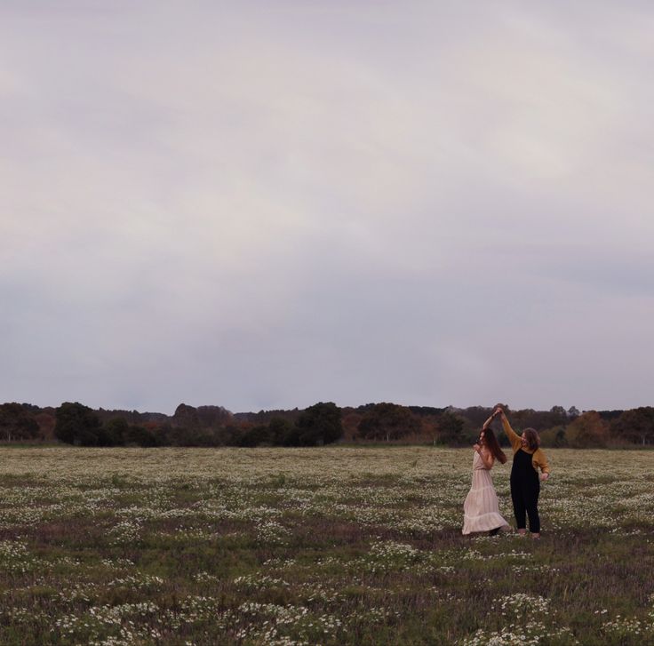 a man and woman standing in the middle of a field with a kite flying above them