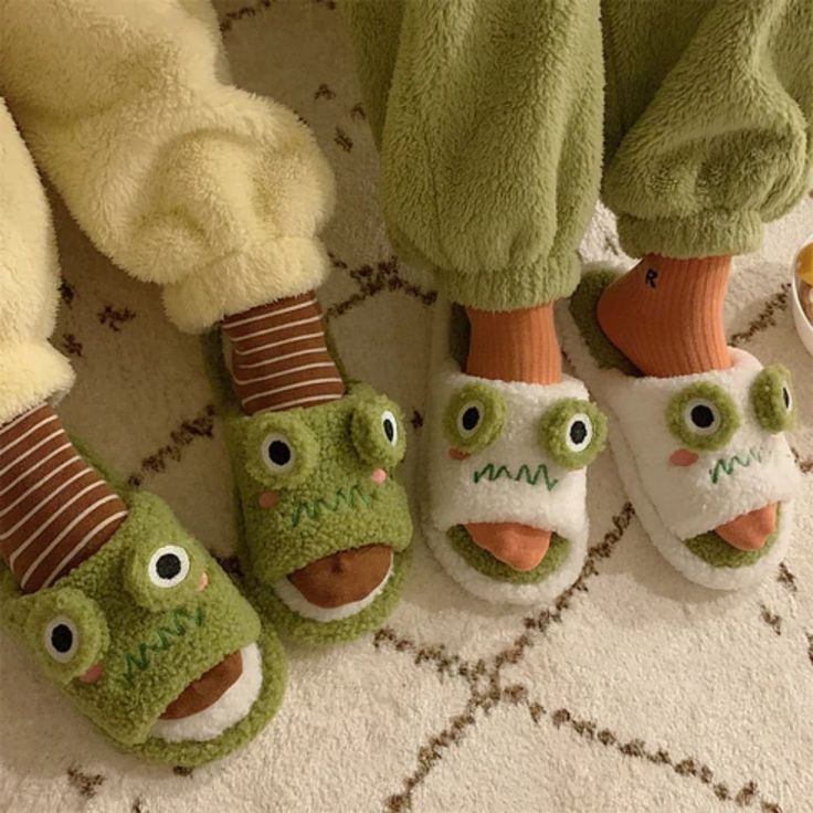 three pairs of slippers with faces on them sitting next to each other in front of stuffed animals