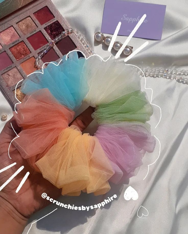 a hand holding a multicolored tulle on top of a white table cloth