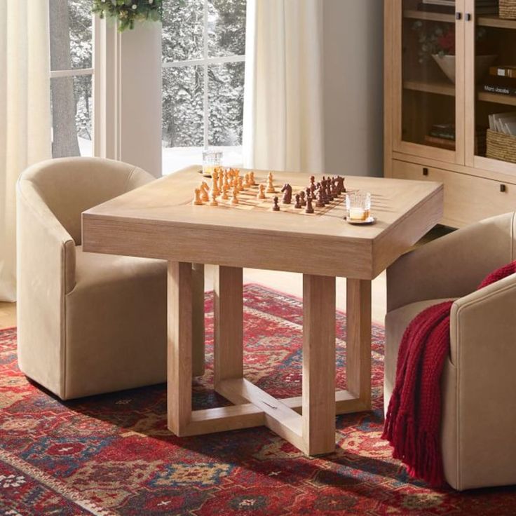 a small table with chess pieces on it in front of a couch and chair next to a window