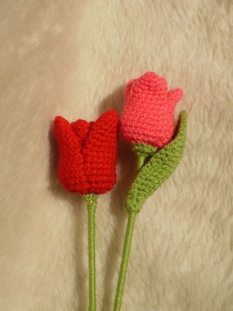 two crocheted flowers sitting next to each other on a white surface with one red flower in the middle